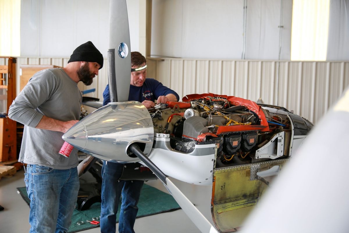 Two technicians working on an engine behind the propeller